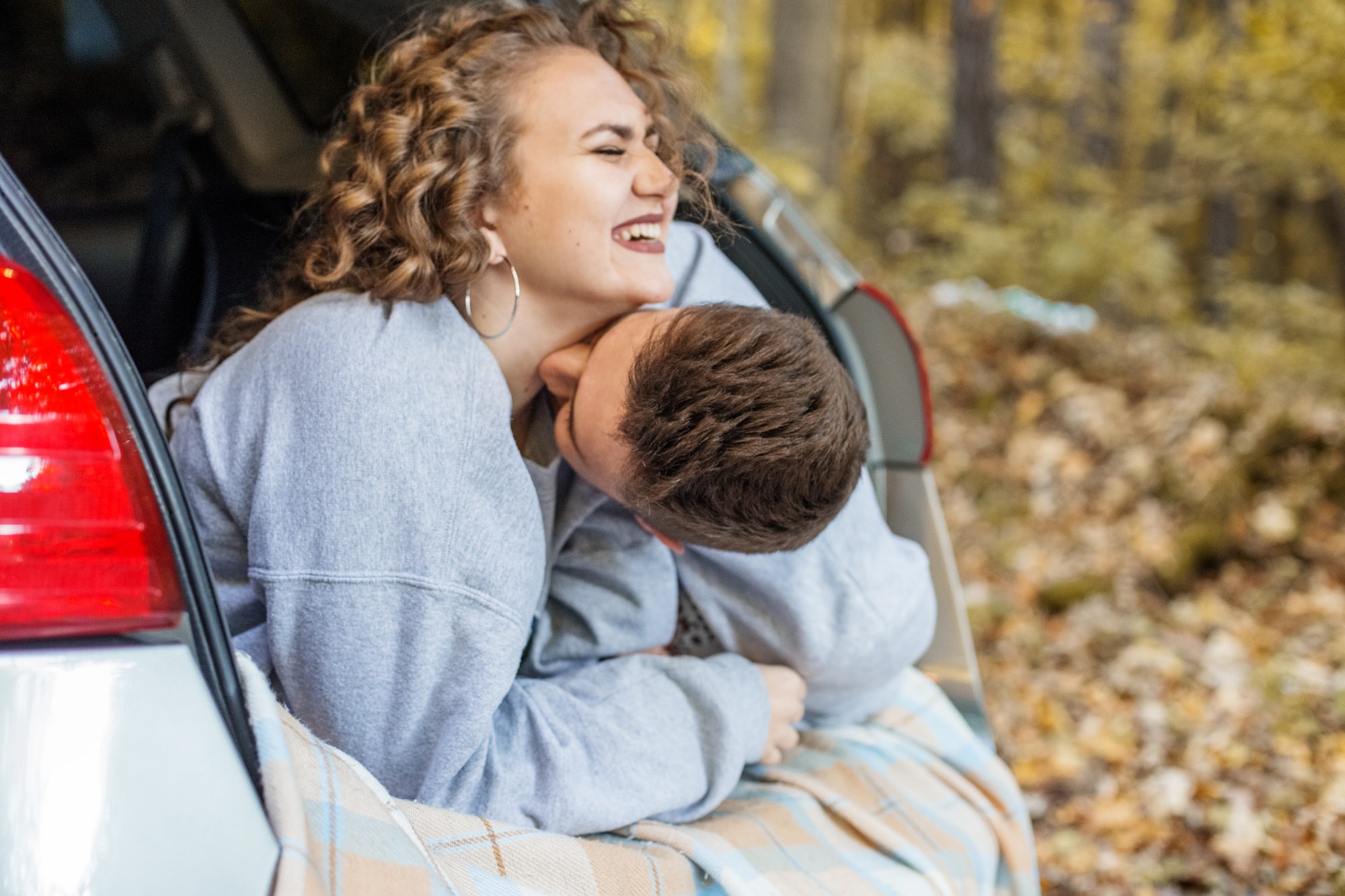 Boy and girl are hugging in trunk of car. Autumn forest. Couple in love. Romantic date.