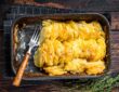 Potato casserole Gratin Dauphinois in a baking dish. Dark wooden background. Top View