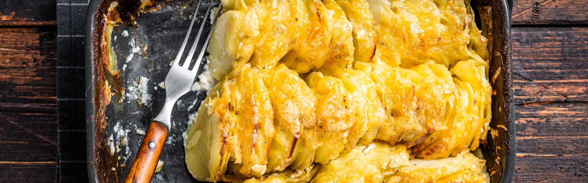 Potato casserole Gratin Dauphinois in a baking dish. Dark wooden background. Top View