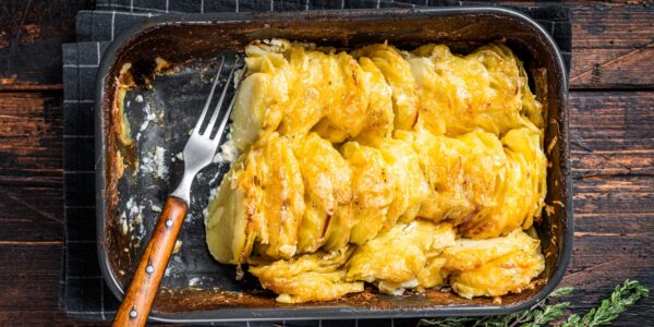 Potato casserole Gratin Dauphinois in a baking dish. Dark wooden background. Top View