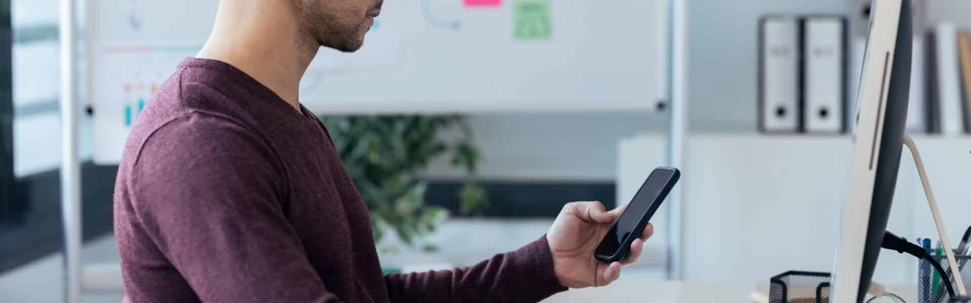 Handsome entrepreneur sending messages with smart phone while working with computer
