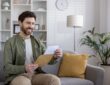 Smiling man reading letter on couch in modern living room