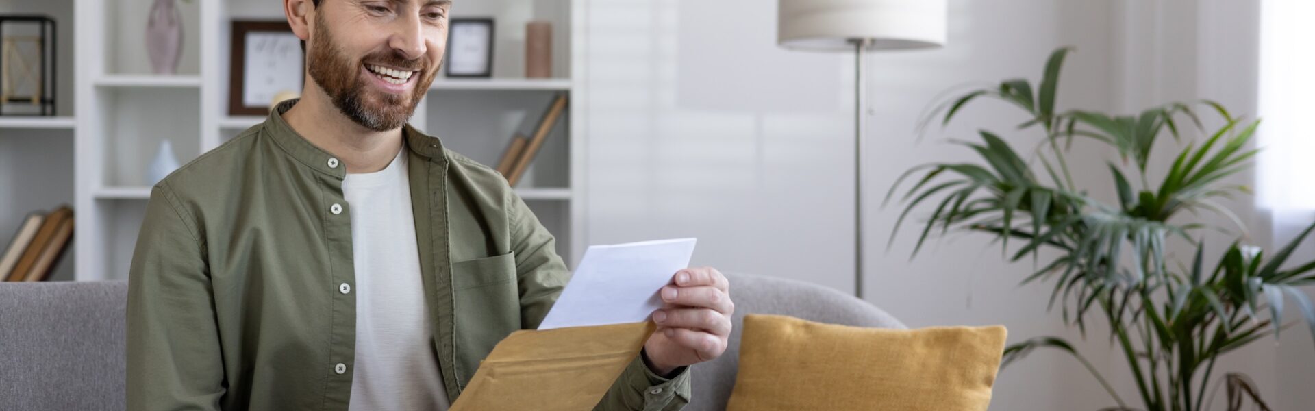 Smiling man reading letter on couch in modern living room